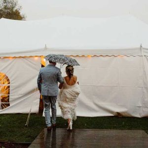 Bride and groom walking into tented reception in the rain